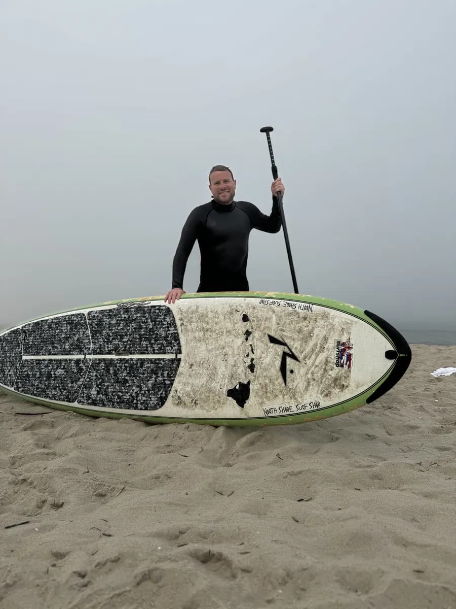 Brent standing on a foggy beach with a paddle and a stand-up paddleboard