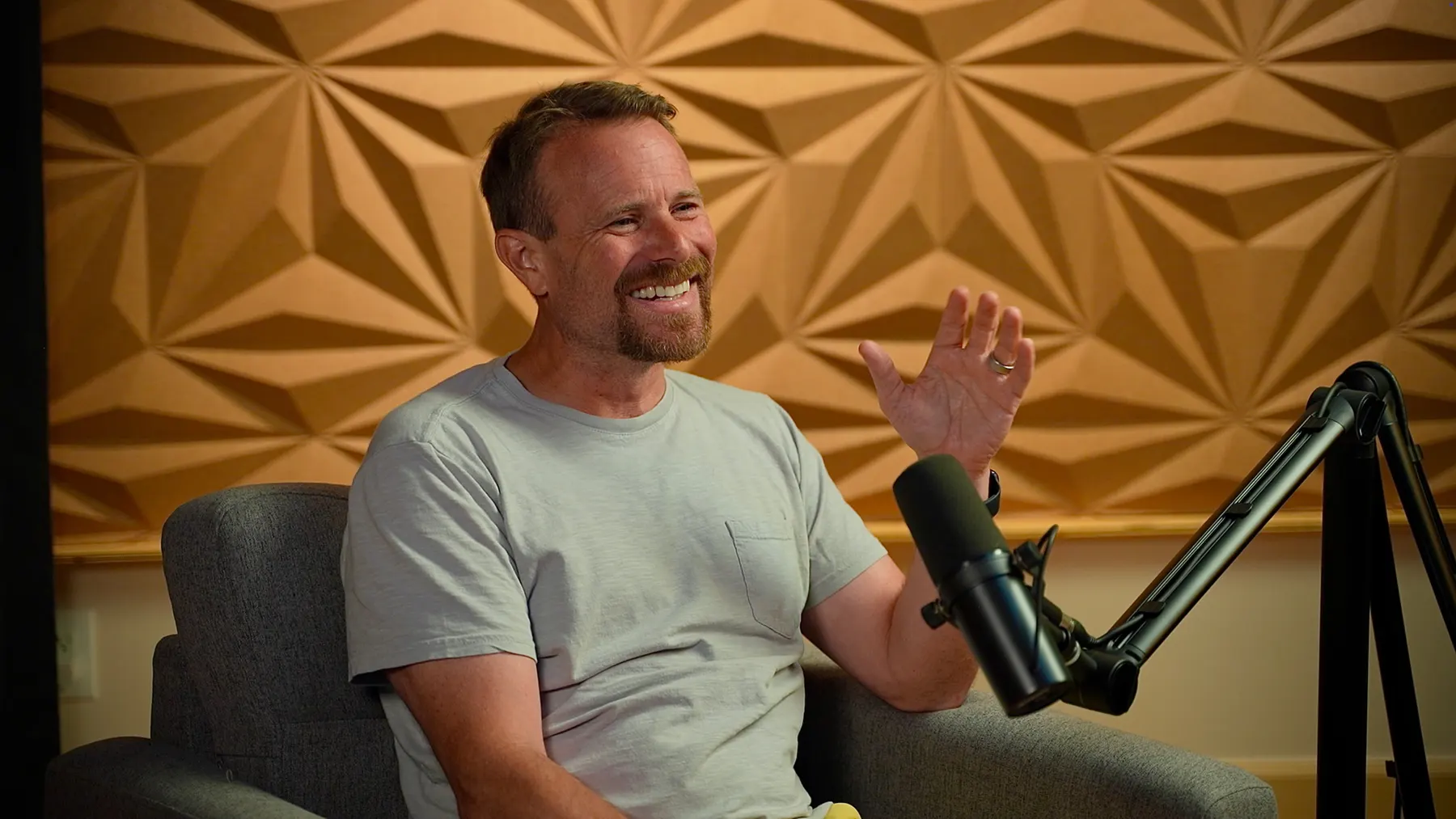 Brent Nickles mid-conversation on a podcast set, gesturing beside a studio microphone