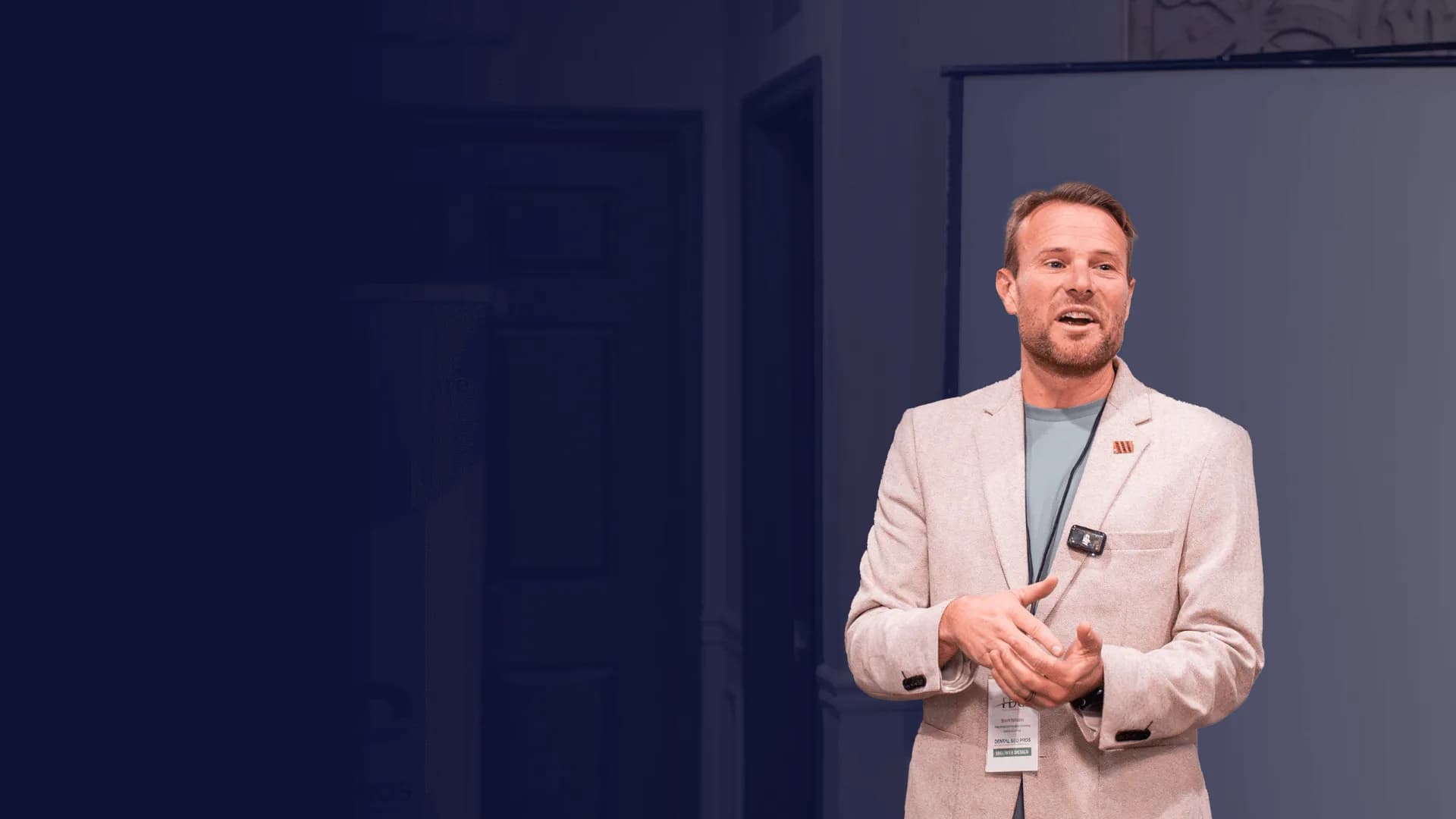Brent Nickles speaking on stage in a light blazer against a deep navy backdrop