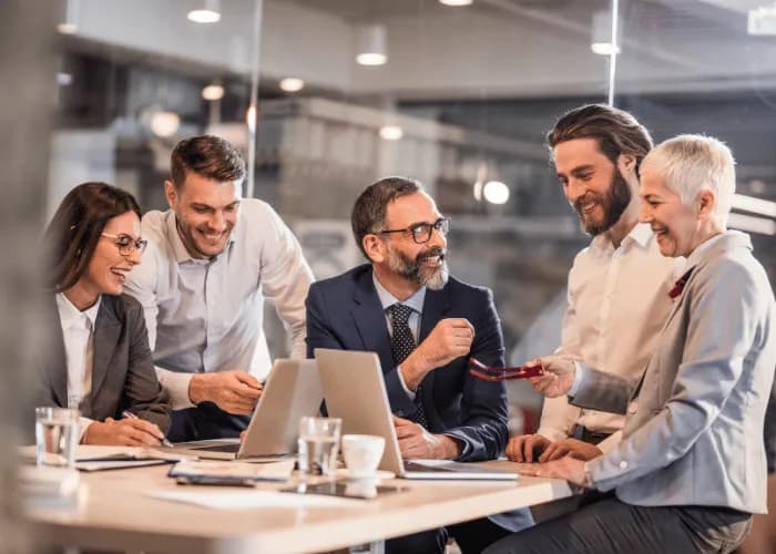 A small team smiling around a meeting table with laptops